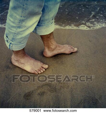 Stock Image - A man walking barefoot on the beach. Fotosearch