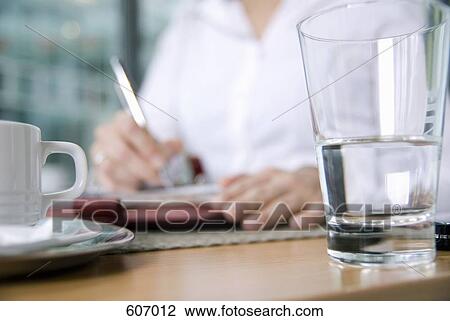 A person sitting at a table with a glass and cup in the foreground View Large Photo Image Stock Image - A person sitting at a table with a glass and cup in the foreground. Fotosearch