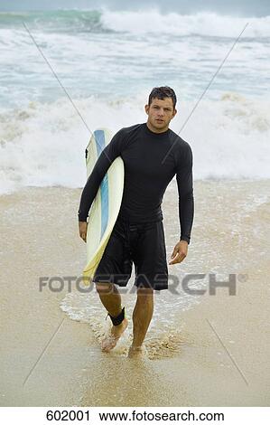 Stock Image - A surfer carrying his surfboard. Fotosearch
