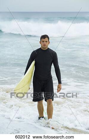 Stock Image - A surfer carrying his surfboard. Fotosearch