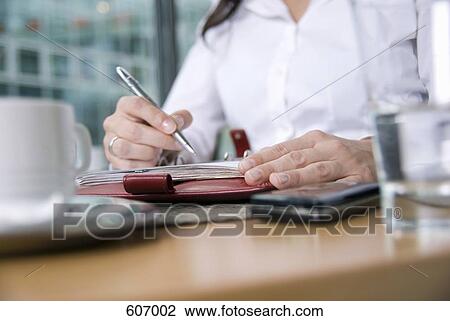 Stock Image - A woman sitting at a desk and using a personal organizer. Fotosearch