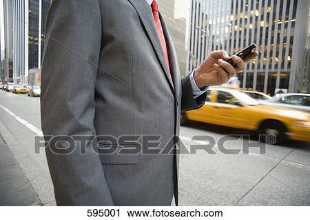 Midsection of a businessman standing on a city street and using a mobile phone View Large Photo Image Stock Image - Midsection of a businessman standing on a city street and using a mobile phone. Fotosearch