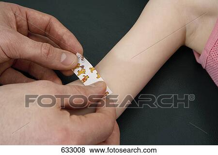 Stock Photo - Human hands putting an adhesive bandage on a child’s arm. Fotosearch