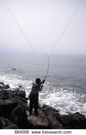 Rear view of a person standing on rocks fishing View Large Photo Image Stock Photograph - Rear view of a person standing on rocks fishing. Fotosearch