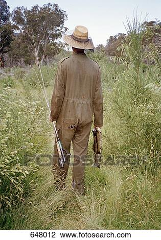 Stock Image - Rearview of a man walking and holding a fishing pole and fish. Fotosearch