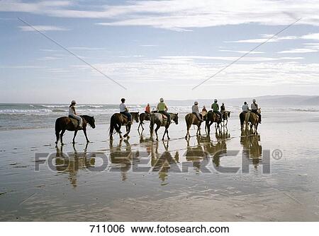 A group of people horseback riding on a beach View Large Photo Image Stock Photograph - A group of people horseback riding on a beach. Fotosearch