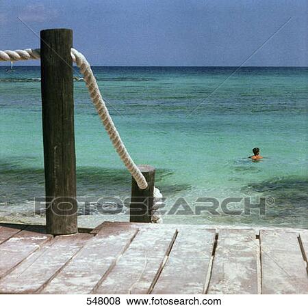 Stock Photo - A rope handrail on a dock and view of a person swimming in the sea. Fotosearch