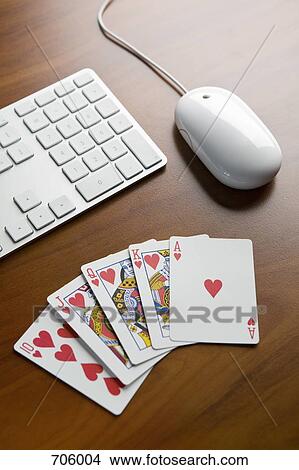 Picture - A royal flush poker hand on a table next to a keyboard and computer mouse. Fotosearch