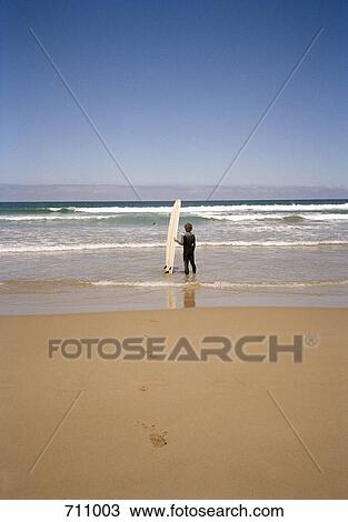 A surfer standing on the beach with his surfboard watching the ocean View Large Photo Image Stock Image - A surfer standing on the beach with his surfboard watching the ocean. Fotosearch