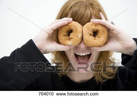 A woman holding up two donuts in front of her eyes View Large Photo Image Stock Image - A woman holding up two donuts in front of her eyes. Fotosearch