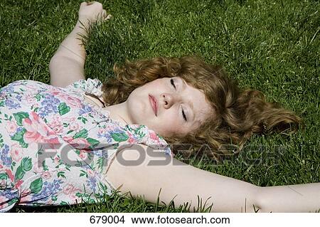 A young woman lying in the grass with her arms stretched out View Large Photo Image Picture - A young woman lying in the grass with her arms stretched out. Fotosearch