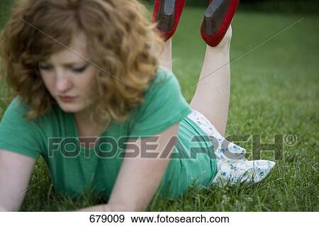 A young woman lying on grass on her front, propped up on her elbows View Large Photo Image Stock Photo - A young woman lying on grass on her front, propped up on her elbows. Fotosearch