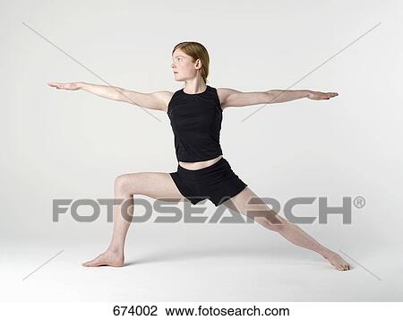 Stock Image - A young woman practicing the 'Warrior II' yoga pose. Fotosearch
