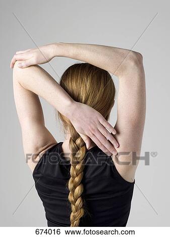 Stock Photograph - A young woman stretching here arm muscles, rear view. Fotosearch
