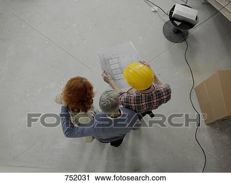 Stock Image - A building contractor going over blueprints with a young couple. Fotosearch