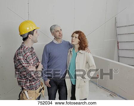 A building contractor talking with a young couple on a building site View Large Photo Image Picture - A building contractor talking with a young couple on a building site. Fotosearch