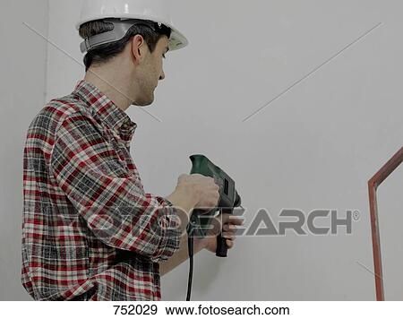 Stock Photo - A construction worker using a drill on a wall. Fotosearch