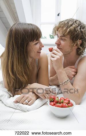 Stock Image - A couple lying on a bed and eating strawberries. Fotosearch