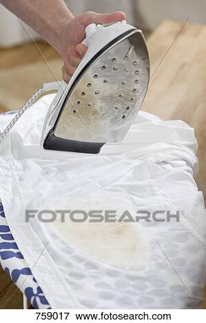 Stock Photo - A human hand holding an iron above a burnt shirt on an ironing board. Fotosearch
