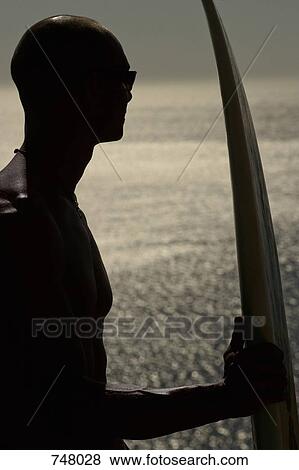Stock Photo - A man by the sea with a surfboard. Fotosearch