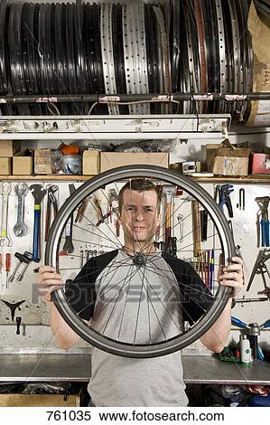 Stock Photography - A man holding a bicycle wheel in a workshop. Fotosearch