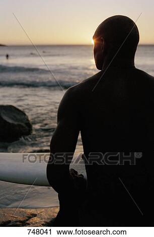 A man sitting by the sea with a surfboard View Large Photo Image Stock Image - A man sitting by the sea with a surfboard. Fotosearch
