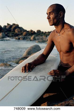 A man sitting by the sea with a surfboard View Large Photo Image Stock Photo - A man sitting by the sea with a surfboard. Fotosearch
