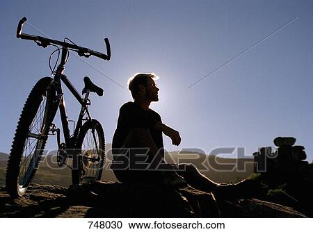 A man sitting on a rock next to a mountain bike View Large Photo Image Stock Image - A man sitting on a rock next to a mountain bike. Fotosearch
