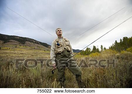 Stock Image - A man standing in a field with a fly rod . Fotosearch