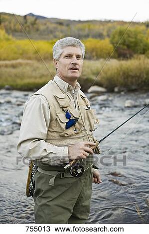 Stock Image - A man standing in a river and holding a fly rod. Fotosearch