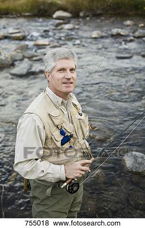 Stock Photo - A man standing in a river and holding a fly rod. Fotosearch