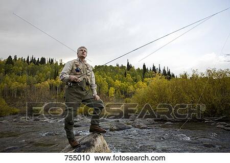 A man standing on a rock while fly fishing in a river View Large Photo Image Stock Image - A man standing on a rock while fly fishing in a river. Fotosearch