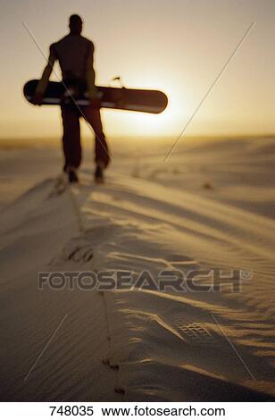 A man standing on a sand dune with a sand board View Large Photo Image Stock Photography - A man standing on a sand dune with a sand board. Fotosearch