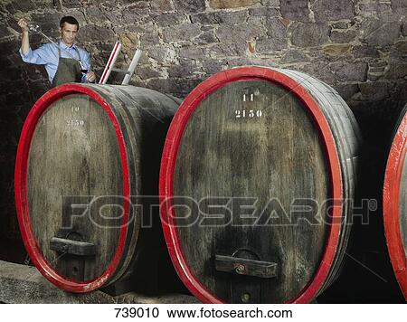 Stock Image - A vintner tests red wine from a barrel. Fotosearch