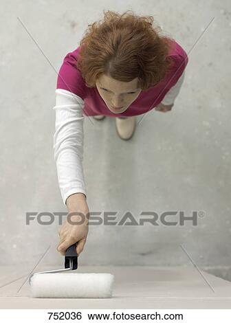 Stock Photograph - A woman painting a wall using a paint roller. Fotosearch