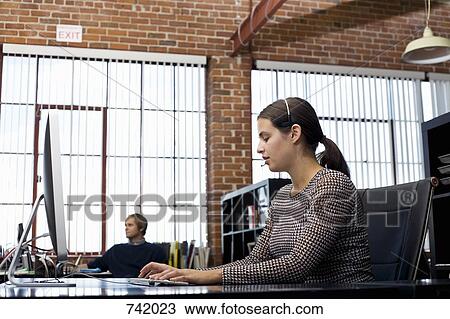 Stock Image - A woman wearing a headset and using a computer in an office. Fotosearch