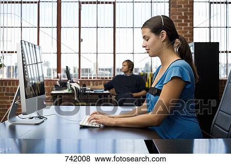 A woman wearing a headset and using a computer in an office View Large Photo Image Stock Photo - A woman wearing a headset and using a computer in an office. Fotosearch