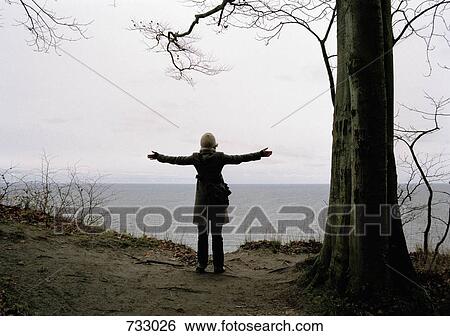 A woman with her arms outstretched facing the sea View Large Photo Image Stock Photograph - A woman with her arms outstretched facing the sea. Fotosearch