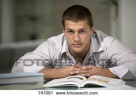 Stock Image - A young man leaning on a desk with an open book. Fotosearch