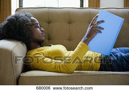 A young woman lying on a couch reading a book View Large Photo Image Stock Photograph - A young woman lying on a couch reading a book. Fotosearch