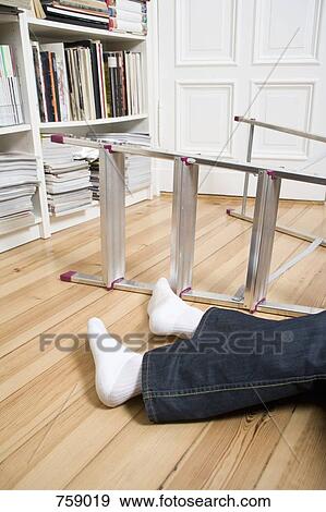 Stock Photo - Human legs lying next to a ladder on its side. Fotosearch