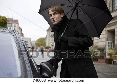 Man holding an umbrella and opening a car door View Large Photo Image Stock Image - Man holding an umbrella and opening a car door. Fotosearch