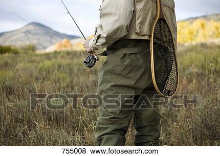 Stock Photo - Midsection of a man holding a fly rod and a fishing net. Fotosearch