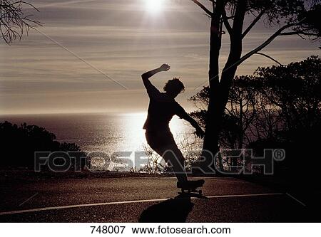 Silhouette of a man riding a skateboard on a road View Large Photo Image Stock Photo - Silhouette of a man riding a skateboard on a road. Fotosearch