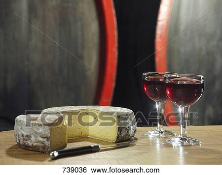 Stock Photograph - Two glasses of red wine and a wheel of cheese, still life. Fotosearch