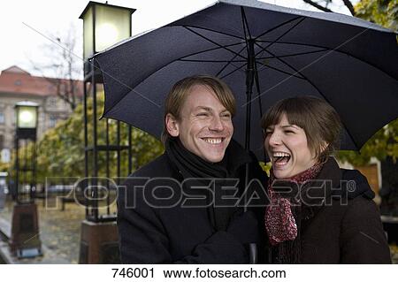 Young couple laughing under an umbrella View Large Photo Image Stock Image - Young couple laughing under an umbrella. Fotosearch