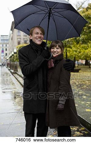 Stock Photograph - Young couple standing and holding umbrellas. Fotosearch