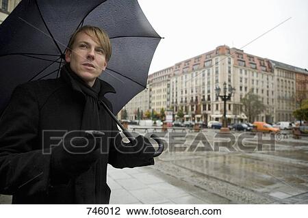 Young man holding a mobile phone and an umbrella View Large Photo Image Stock Image - Young man holding a mobile phone and an umbrella. Fotosearch