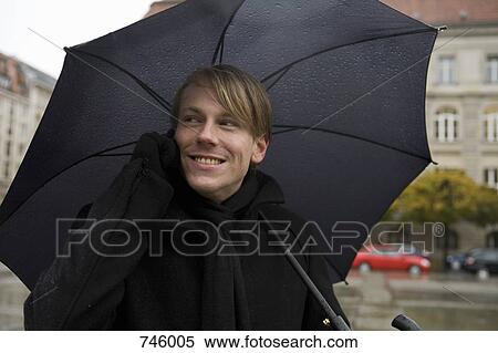 Young man using a mobile phone and holding an umbrella View Large Photo Image Stock Photography - Young man using a mobile phone and holding an umbrella. Fotosearch