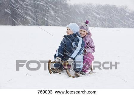 Stock Image - A brother and sister sitting on a sled together tobogganing. Fotosearch